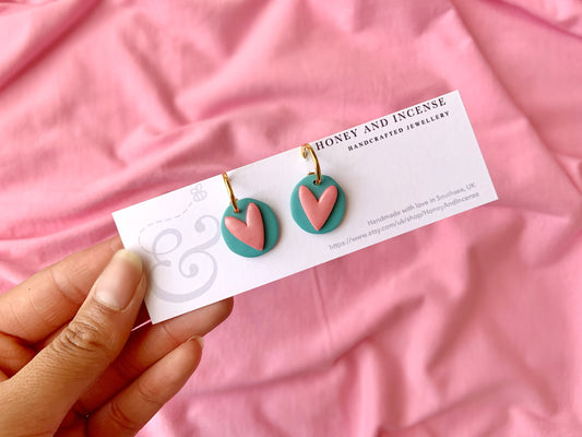 polymer clay charms of a turquoise circle with a pale shimmery pink heart on huggie hoops, pink doll vibe earrings