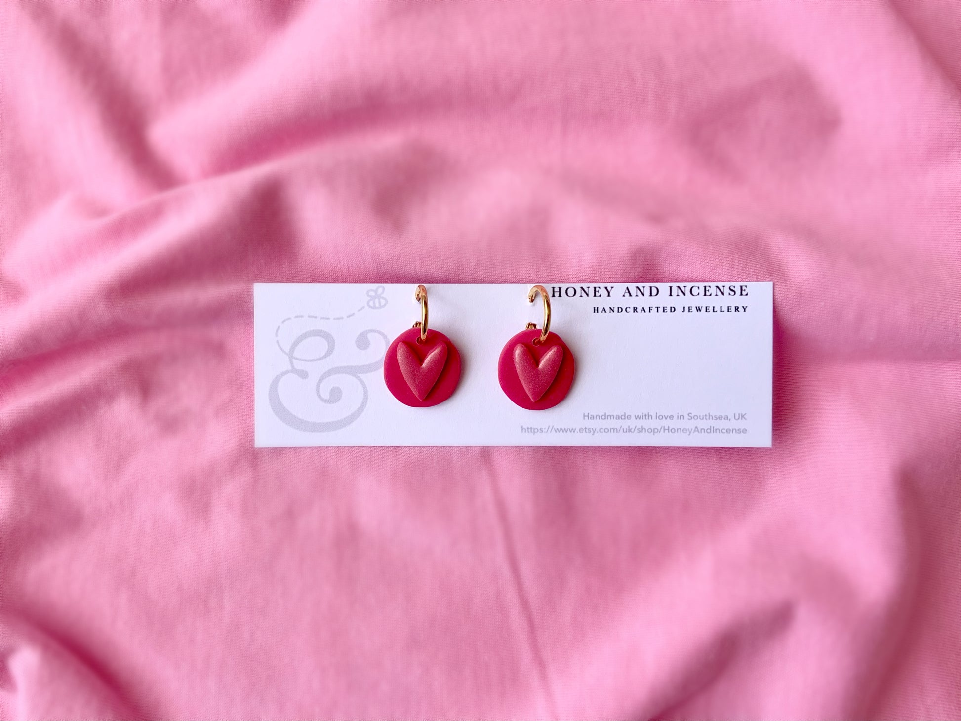 gold huggie hoops with hot pink polymer clay charms on and a shimmery pink heart