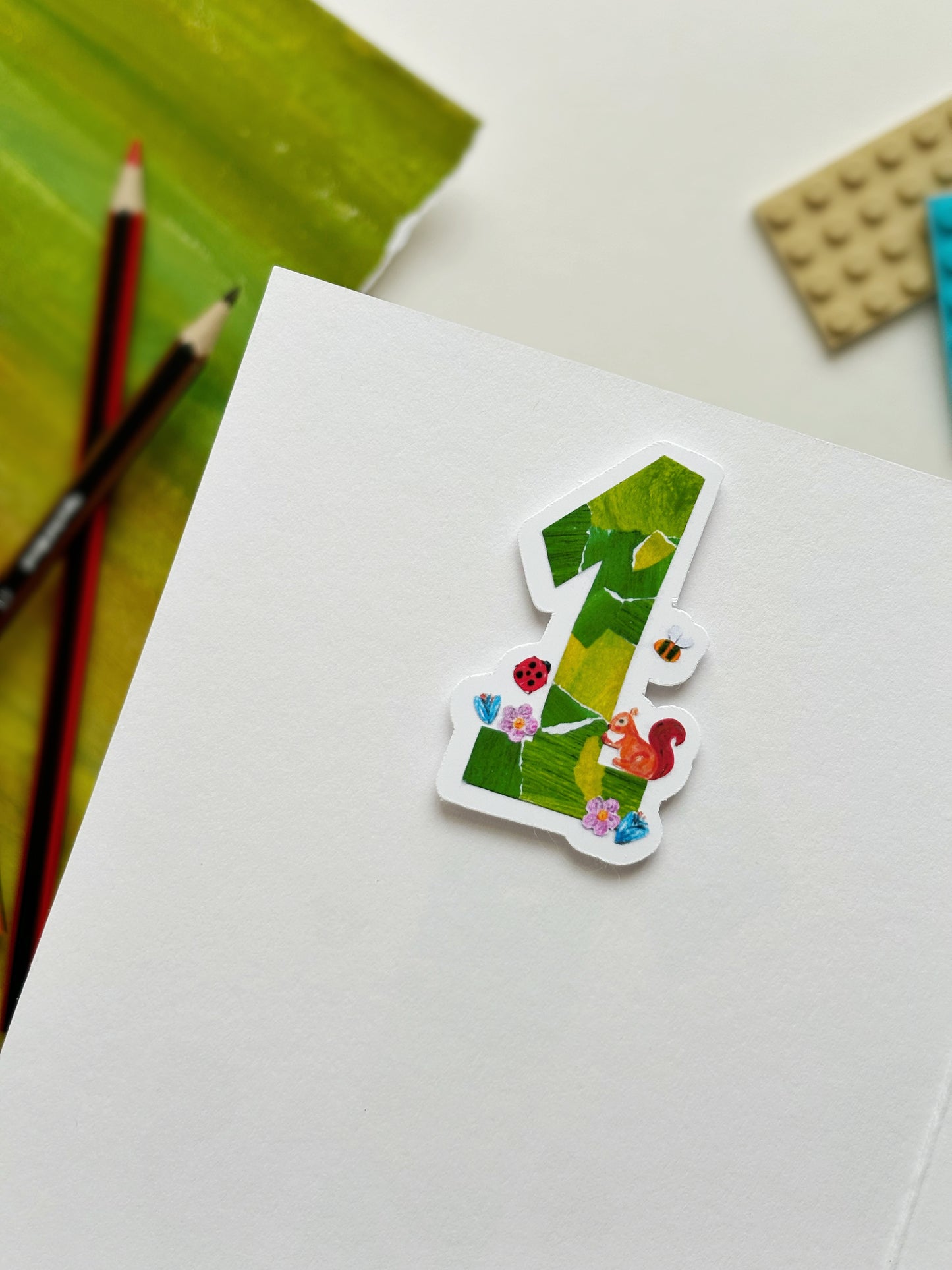 Age 1 sticker in a birthday card, the sticker is a green 1 made from collage materials and bees and ladybird cut outs 