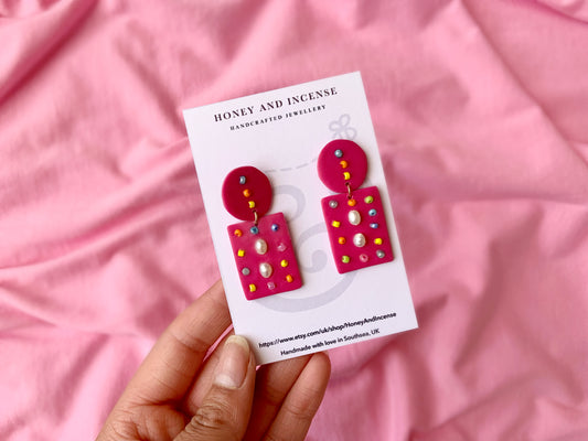 Hot pink polymer clay earrings with pearls embedded into them, and colourful glass beads dotted around