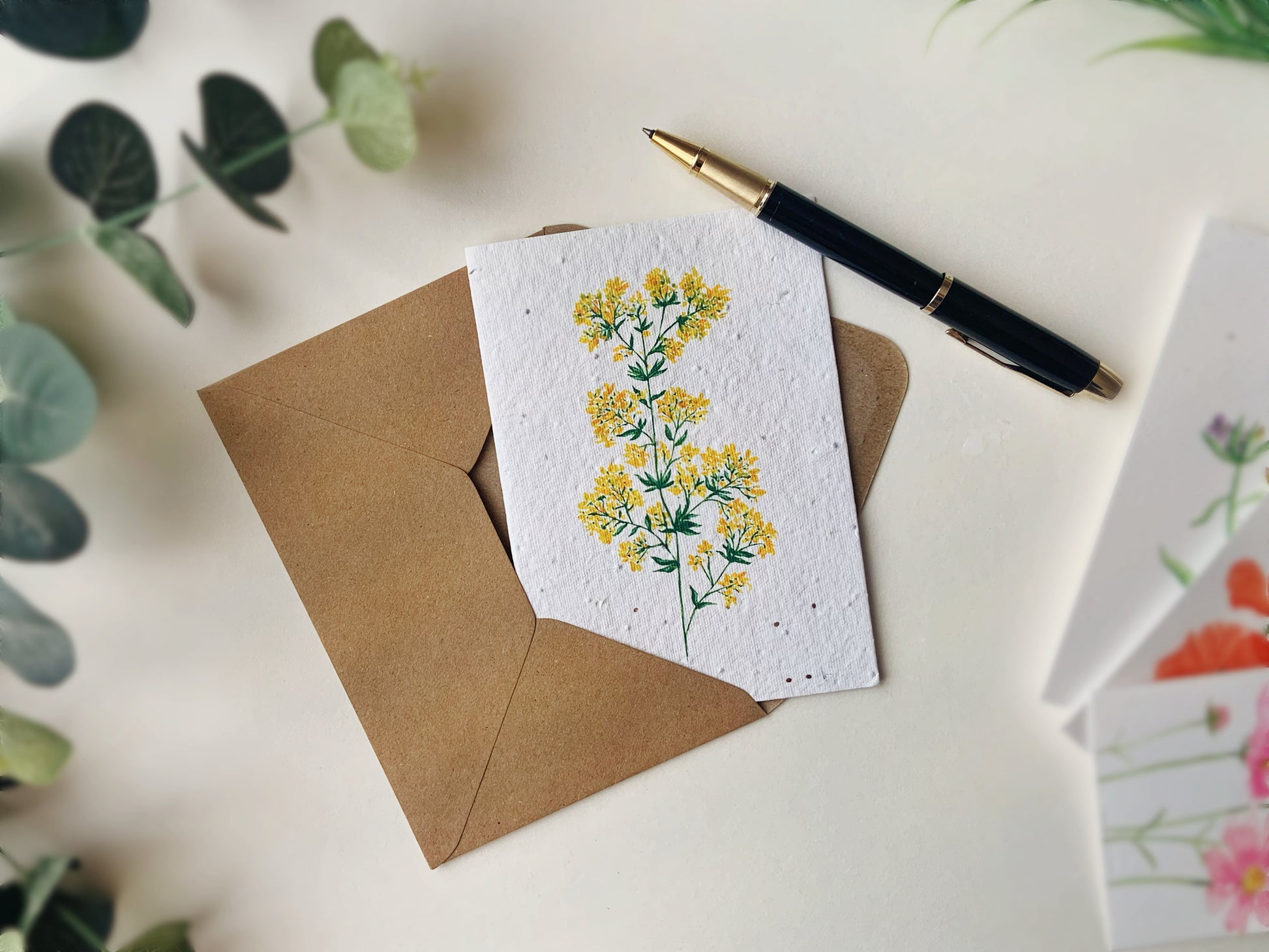 yellow wildflower seeded card, on a blurred background with a parker pen and eucalyptus leaf