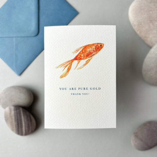 Card with goldfish illustration and text 'You are pure gold, thank you' on a stone surface.