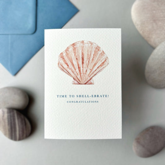 Greeting card with shell illustration and text, surrounded by stones and a blue envelope.