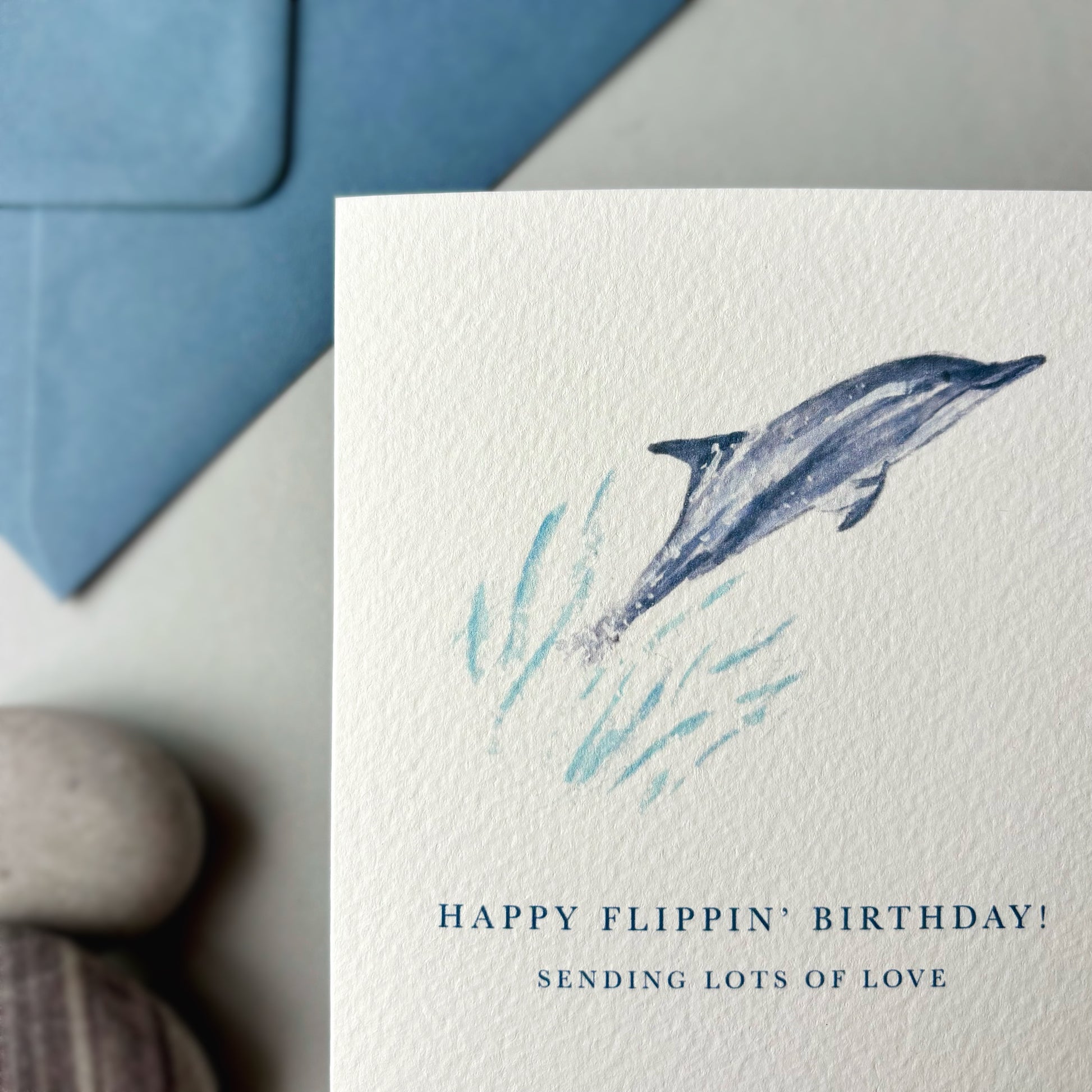 Greeting card with a dolphin illustration and humorous birthday message on a neutral background.