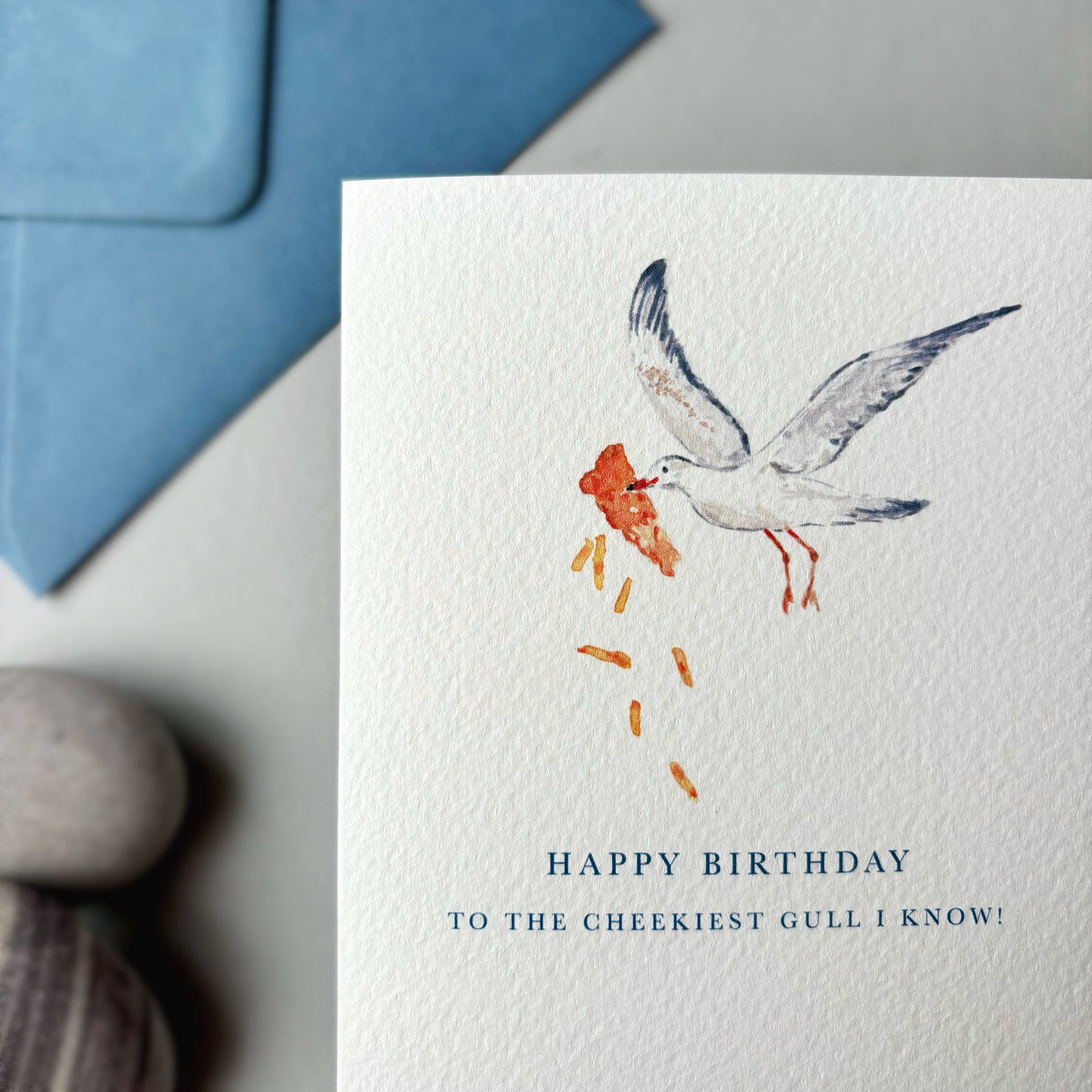 Birthday card with a seagull illustration and blue envelope on a neutral background