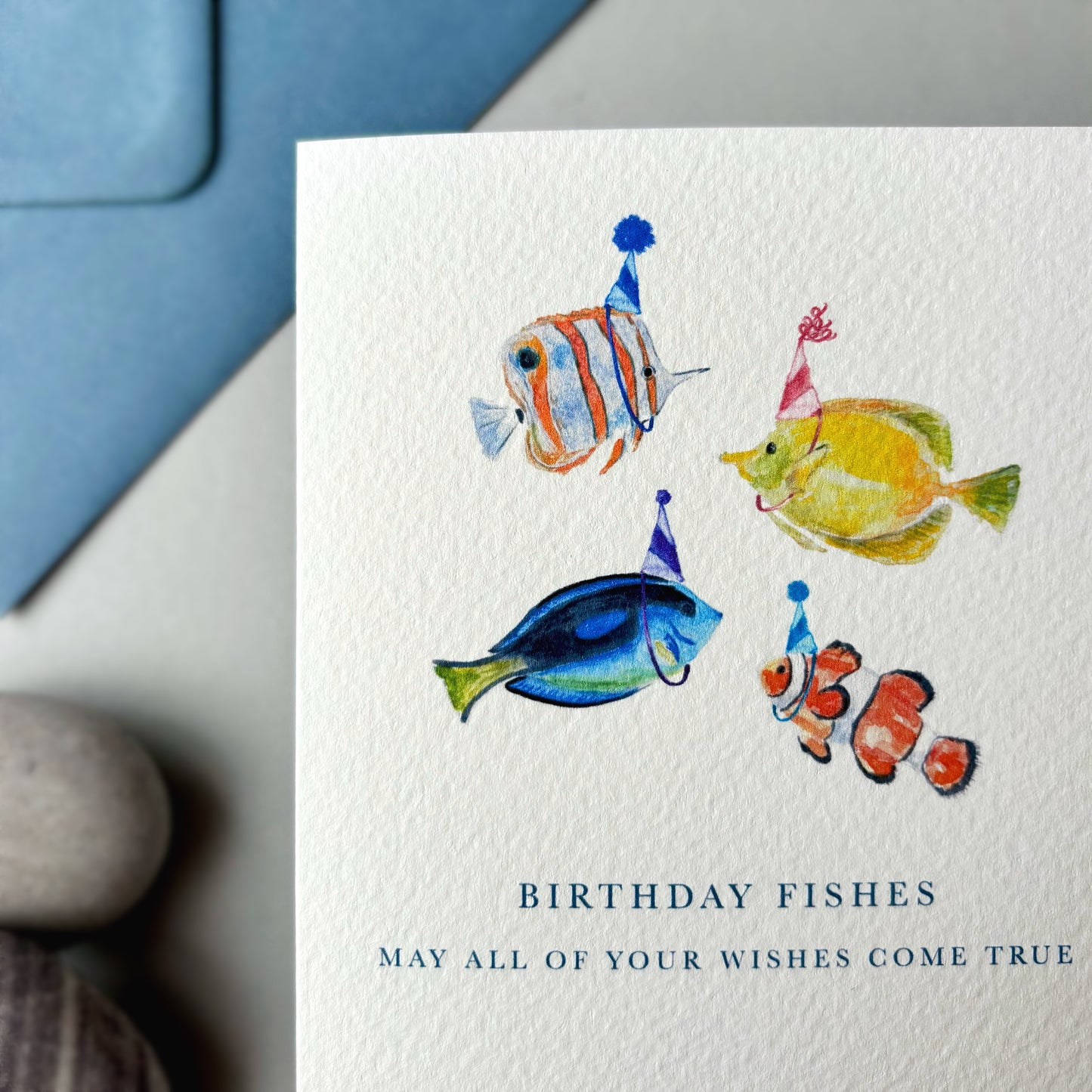 Birthday card with watercolor fish illustrations and text 'Birthday Fishes' on a textured surface.