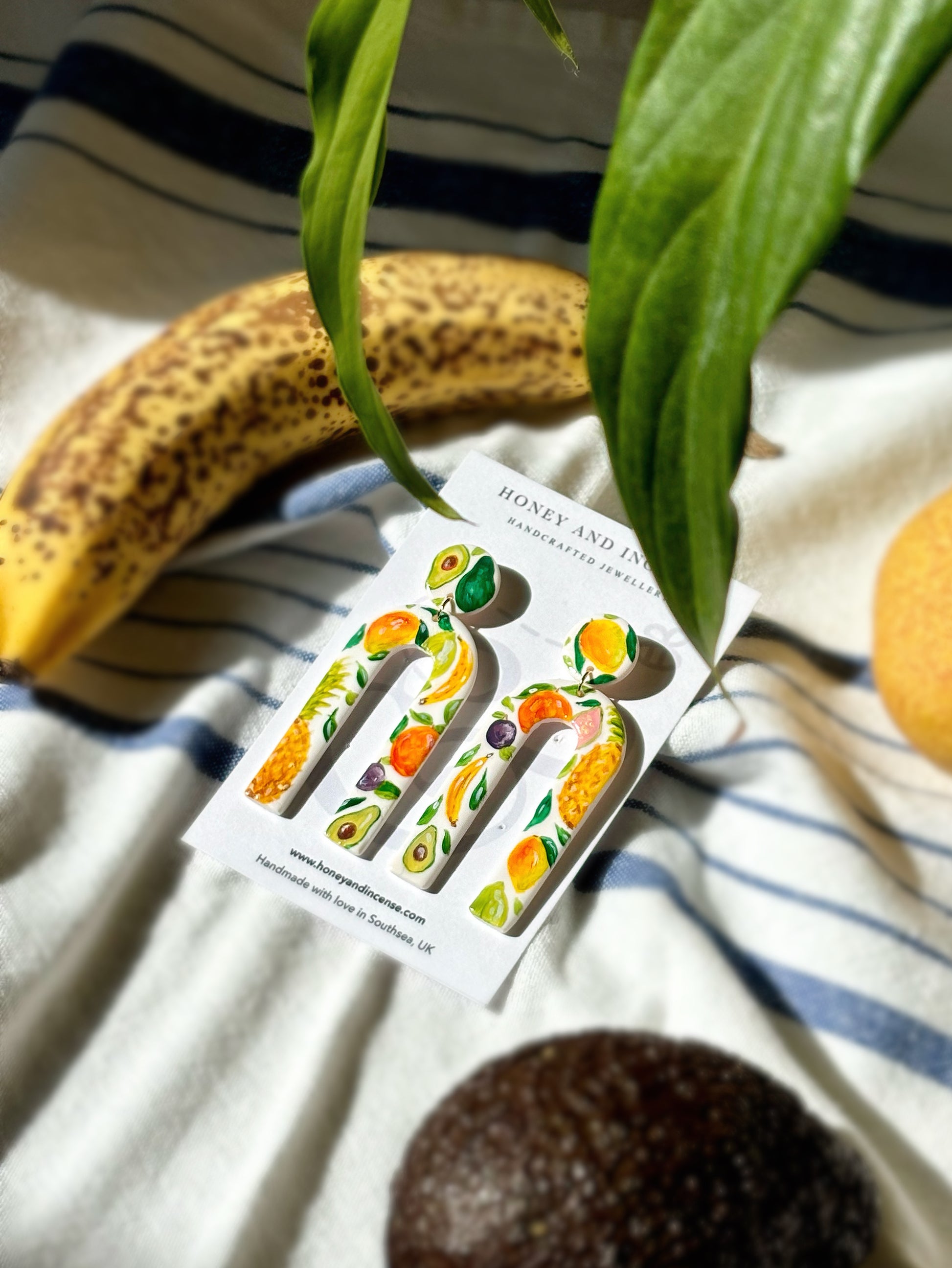 Hand painted polymer clay earrings with tropical fruit on them including avocados and pineapple